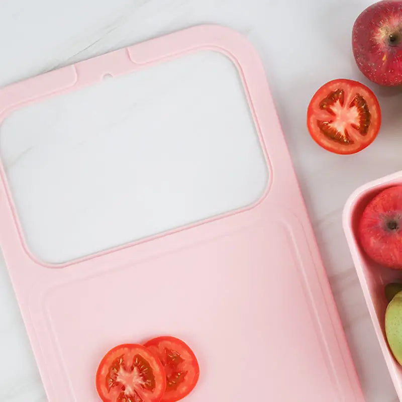 Pink Multifunctional Sink Chopping Board with Drain Basket taken out, with sliced tomatoes and whole apples on a light surface