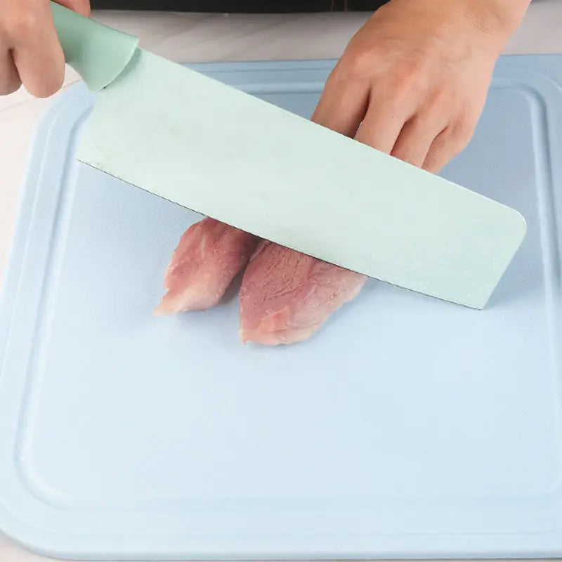 Person using a green knife to cut a piece of meat on a blue cutting board.