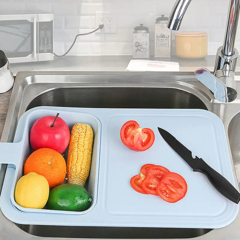 Multifunctional Sink Chopping Board with Drain Basket, with fruits and vegetables in the basket and on the board across a kitchen sink