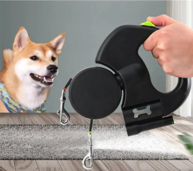 Black Auto Double Dog Leash retractable with a hand holding it, next to a dog on a wooden floor.